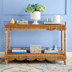 a wicker shelf with books and flowers on it in front of a blue wall