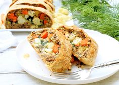 a white plate topped with meat filled pastry next to a pile of potatoes and carrots