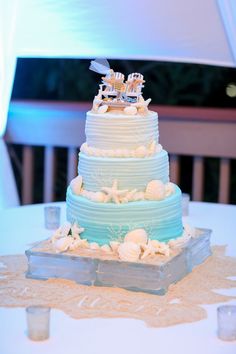 a three tiered blue and white wedding cake with sea shells on the bottom layer