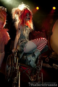 two women dressed as clowns on stage with one sitting in a wheel chair and the other standing