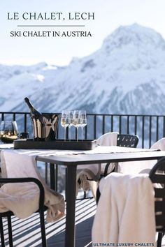 an outdoor table with wine glasses and bottles on it in front of a snowy mountain