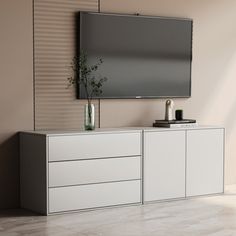 a tv mounted to the side of a wall next to a white cabinet with drawers