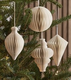 three white paper ornaments hanging from a christmas tree with pine branches in the foreground