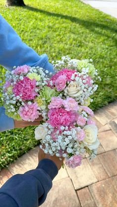 a person holding a bouquet of pink and white flowers in their hand on a brick walkway