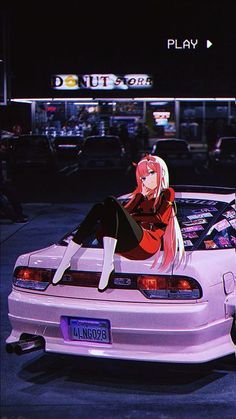 a woman sitting on the back of a pink car in front of a building at night