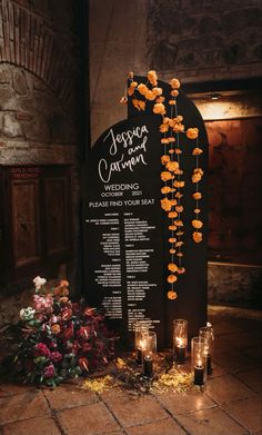 a wedding ceremony sign with candles and flowers on the ground in front of an arch