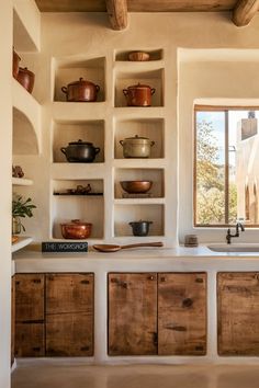 a kitchen filled with lots of wooden cupboards and pots on top of shelves next to a window