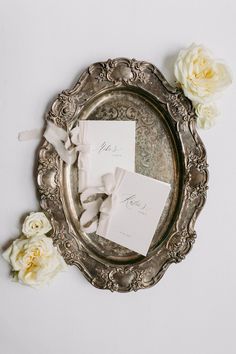 the wedding stationery is laid out in an ornate silver frame with flowers on it