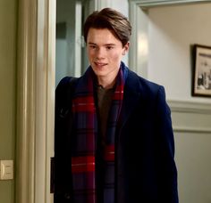 the young man is wearing a red and black plaid scarf as he stands in front of an open door