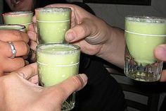 several people holding glasses filled with green liquid