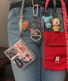 a woman holding a red purse with several keychains attached to it and two small bears in the pocket