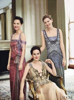 three women in evening gowns posing for a photo with one sitting on a chair