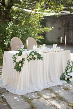 a table with white flowers and greenery on it is set for an outdoor dinner