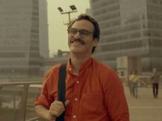 a man in an orange shirt is holding a black bag and smiling at the camera