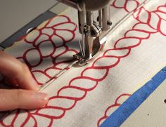 someone is using a sewing machine to sew something on a tablecloth with red and blue designs