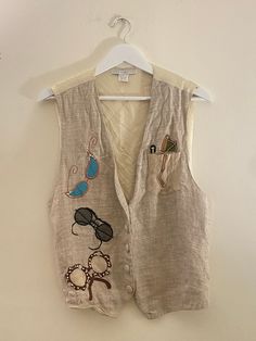 Super cute vintage 90s Y2K beige linen and silk vest with front pocket buttons and tie back waist  Features a funky embroidered sunglasses print with beaded and rhinestone details  Vest is One Size  In great vintage condition!  Pair with light wash baggy denim, Birkenstocks, and wayfarers for a cool bohemian retro look Spring Linen Beach Vest, Trendy Beige Summer Vest, Bohemian Style Summer Vest For Day Out, Retro Fitted Summer Vest, Retro Fitted Vest For Summer, Summer Linen Vest With Pockets, Trendy Summer Vest With Pockets, Bohemian Vest With Pockets For Spring, Bohemian Spring Vest With Pockets