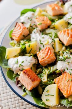 a salad with salmon, potatoes and spinach on a white plate next to a glass of water