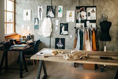 a room with clothes hanging on the wall and desk in front of it, next to a window