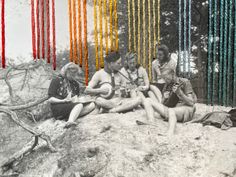 four people sitting on the ground in front of colorful string art hanging from trees behind them