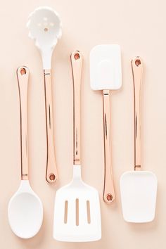 five kitchen utensils lined up on a pink surface