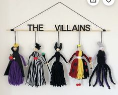 several dolls hanging from a wooden sign that says the villain's