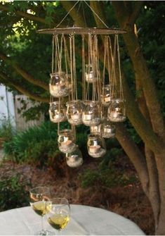 a chandelier hanging from a tree with wine glasses in front of it on a table