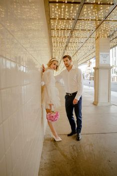 a man and woman standing next to each other near a wall with lights on it