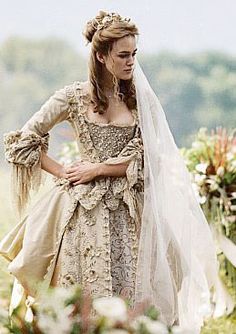 a woman dressed in an old fashion wedding gown and veil walking down the aisle with her hand on her hip