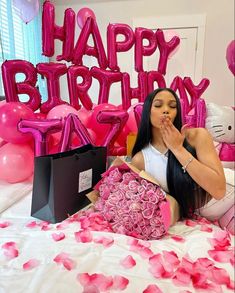 a woman sitting on top of a bed with pink balloons and flowers in front of her