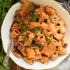 a white bowl filled with pasta covered in sauce and parsley on top of a table