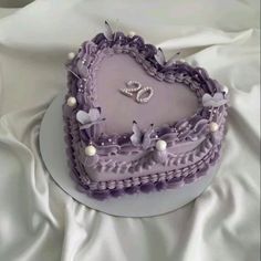 a purple heart shaped cake on a white tablecloth with pearls and butterflies around it