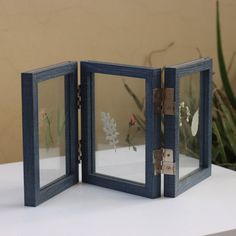 two small mirrors sitting on top of a white table next to a potted plant