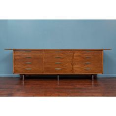 an old wooden dresser with six drawers and two metal pulls on the bottom, against a blue wall