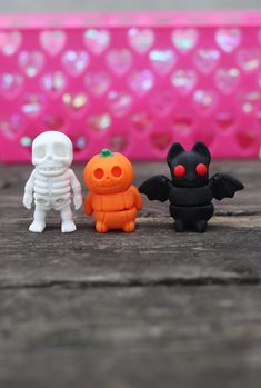 three small toy figurines sitting next to each other on a wooden table in front of a pink background