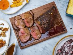 sliced up meat on a cutting board next to other plates and utensils with sauces