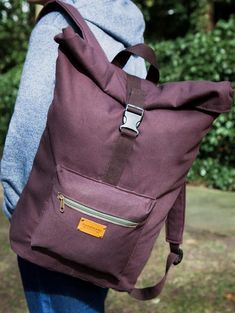 a person carrying a purple backpack with trees in the back ground and bushes behind them