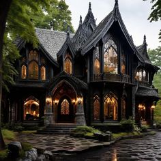 a gothic - style house is lit up at night in the rain, surrounded by trees and rocks