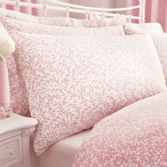 a bed with pink and white flowers on the pillow cases, along with two nightstands