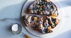 a white plate topped with a cake covered in blueberries and other toppings next to a spoon