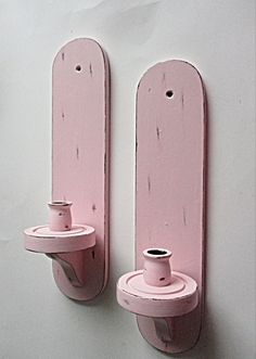 two pink wall mounted toothbrush holders on the side of a white wall, one holding a cup