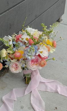 a bouquet of flowers sitting on the ground next to a wall with a pink ribbon tied around it