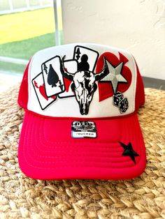 This trendy red and white trucker hat features an eye-catching design with a winning hand of aces, a bold bull skull, and lucky dice, making it the perfect accessory for country lovers, rodeo fans. Fun Adjustable Trucker Hat For Rodeo, Red Trucker Hat For Rodeo, Red Snapback Hat For Rodeo, Red Snapback Trucker Hat For Rodeo, Western Style Trucker Hat For Western-themed Events, Western Themed Snapback Trucker Hat, Country Style Trucker Hat For Western-themed Events, Novelty Red Trucker Hat, Red Trucker Hat