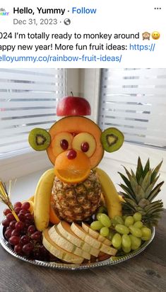 a plate filled with fruit and a monkey made out of bananas, apples, grapes, and pineapples