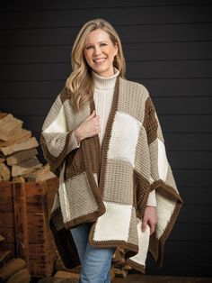 a woman standing in front of stacks of logs wearing a brown and white crocheted ponchy