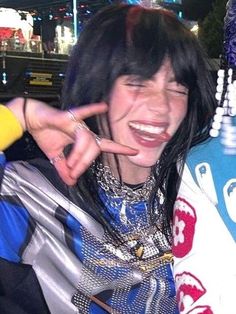 a woman with black hair and piercings making the peace sign