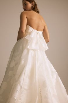 a woman in a white wedding dress with a big bow on it's back