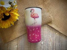 a pink and white cup with a flamingo painted on it next to sunflowers