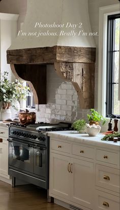 a kitchen with white cabinets and an old - fashioned stove hood in the center, surrounded by potted plants