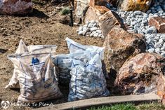 three bags of gravel sitting on the ground next to some rocks