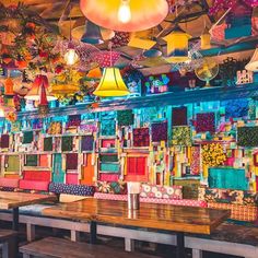 a colorful restaurant with wooden tables and chairs in front of the wall is decorated with brightly colored fabrics